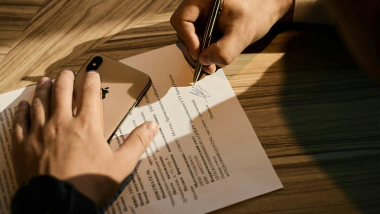 Pessoa escrevendo em documento sobre a mesa, representando o aditivo de reequilíbrio de contrato público