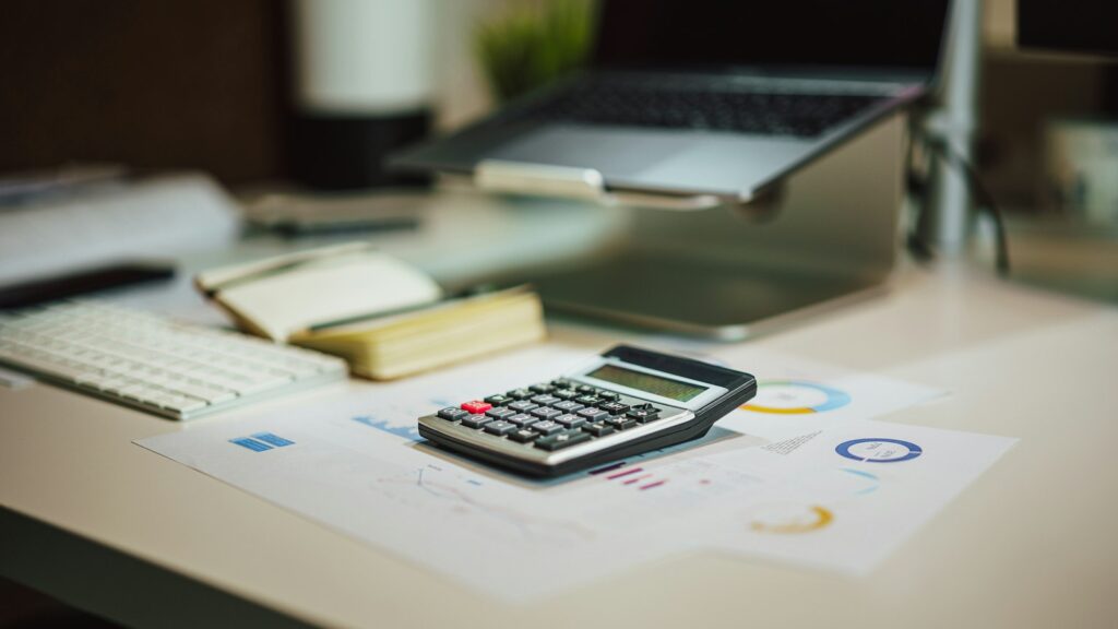Calculadora ao lado de laptop sobre a mesa, usada para calcular o custo da redução da jornada de 44 para 40 horas