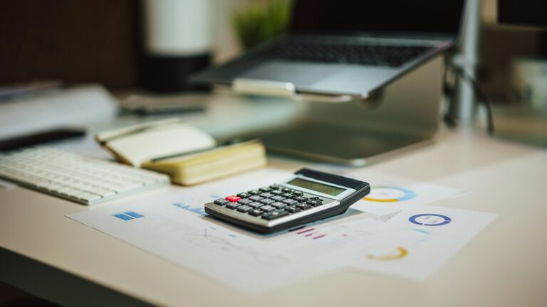 Calculadora ao lado de laptop sobre a mesa, usada para calcular o custo da redução da jornada de 44 para 40 horas