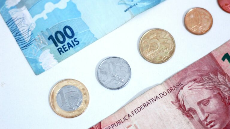 Cédulas e moedas de real sobre a mesa, representando a carga tributária brasileira de 32,4% do PIB em 2025