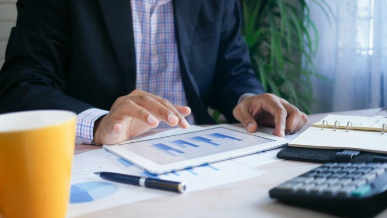 Executivo analisando números em tablet e calculadora, avaliando o capital de giro diante da nova jornada