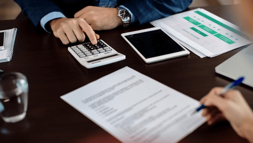 Mão preenchendo documentos ao lado de calculadora, ilustrando a revisão de contribuições previdenciárias